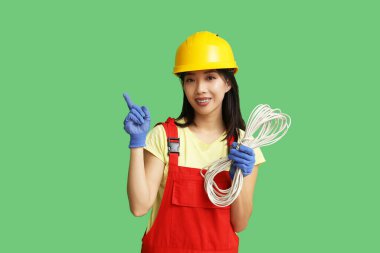 Kabloları yeşil arka plandaki bir şeyi gösteren genç bir elektrikçi.