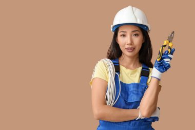 Bej arka planda pense ve kabloyla genç bayan elektrikçi.