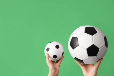 Yeşil arka planda futbol topları olan kadın eller.