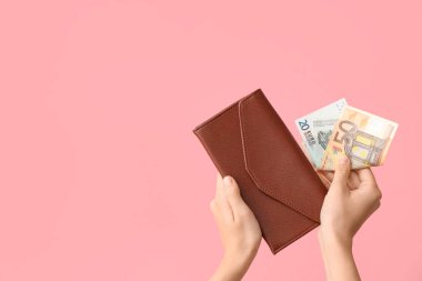 Cüzdanı ve parası pembe arka planda olan kadın elleri.
