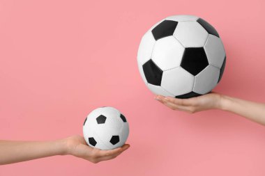 Pembe arka planda futbol topları olan kadın eller.