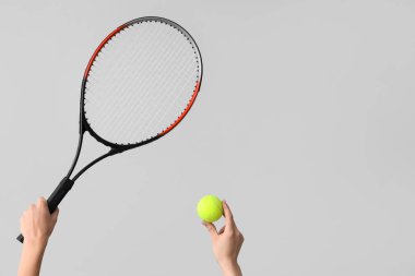 Gri arka planda tenis topu ve raketi olan kadın eller.