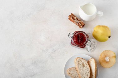 Tatlı reçelli lezzetli kahvaltı, ayva meyvesi, ekmek parçaları ve beyaz masada bir sürahi süt.