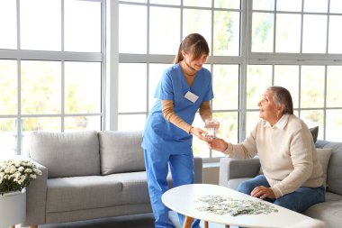 Yaşlı kadın evde bakıcıdan bir bardak su alıyor.