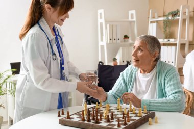 Yaşlı kadın huzurevindeki doktordan bir bardak su alıyor.