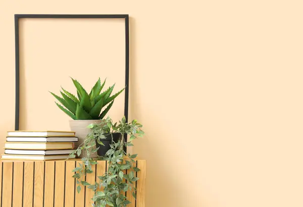 Wooden cabinet with houseplants and books near beige wall