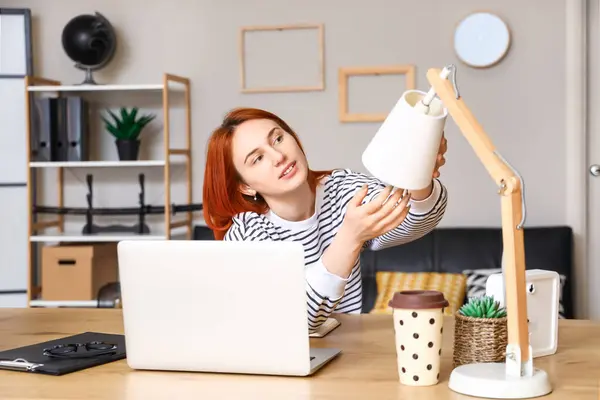 Pretty young woman changing light bulb in desk lamp at home