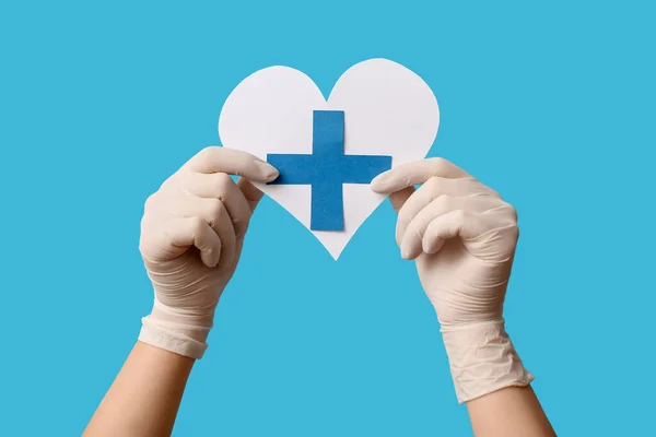 Doctor with paper cross and heart on blue background