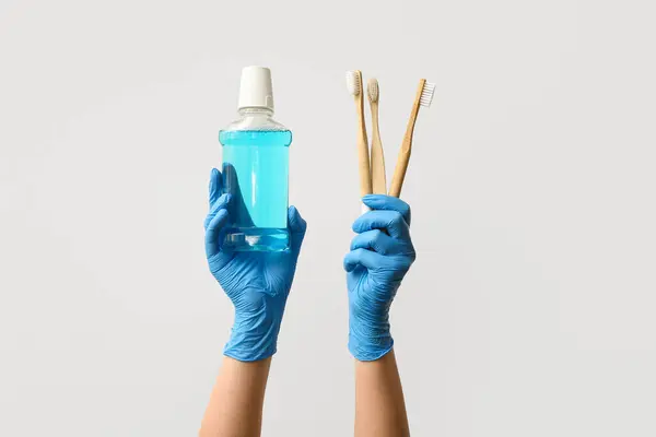 Woman with mouth rinse and toothbrushes on light background