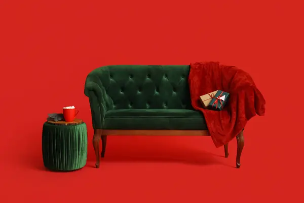 Modern green sofa with blanket and ottoman on red background
