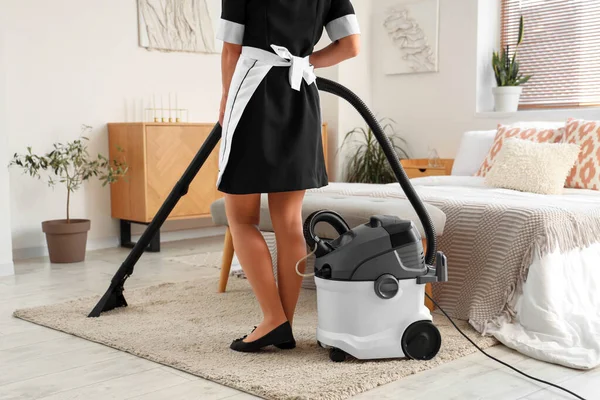 Chambermaid cleaning hotel room with vacuum cleaner