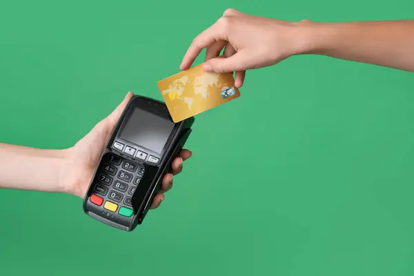 Female hands with payment terminal and credit card on green background