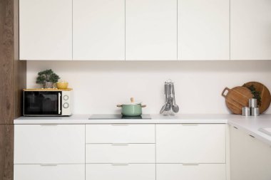 Mikrodalga fırını, elektrikli soba ve beyaz tezgahlı mutfak malzemeleri.