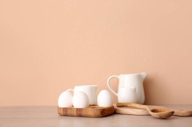 Mutfak gereçleri ve yumurtalar bej duvarın yanındaki ahşap masada.