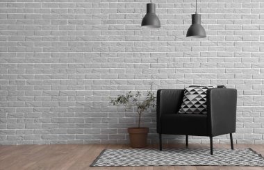 Gri tuğla duvarın yanında yastıklı siyah koltuk