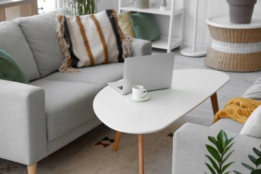 Oturma odasının içinde dizüstü bilgisayarı ve gri kanepesi olan kahve masası.