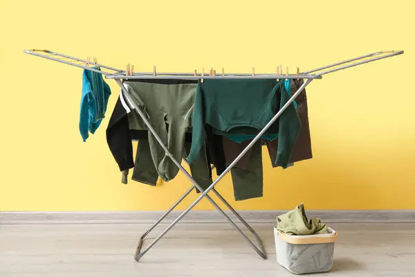 Clean clothes hanging on dryer near yellow wall
