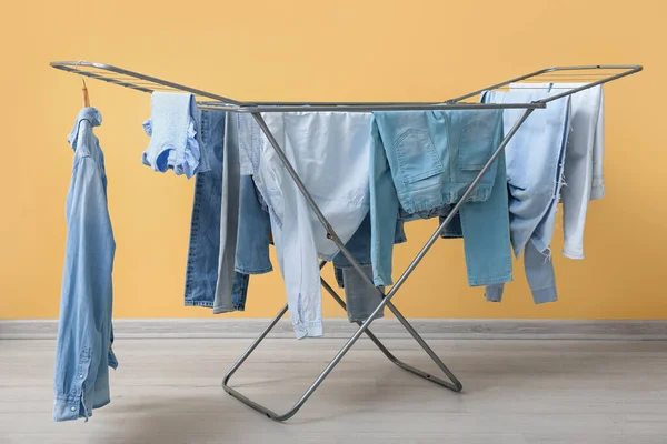 Clean clothes hanging on dryer near yellow wall