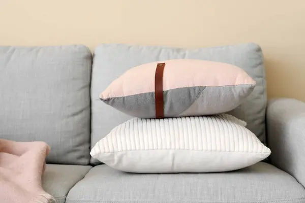 Cozy grey sofa with cushions near beige wall, closeup