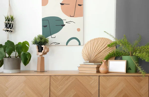 Wooden cabinet with houseplant, books and decor in interior of living room, closeup