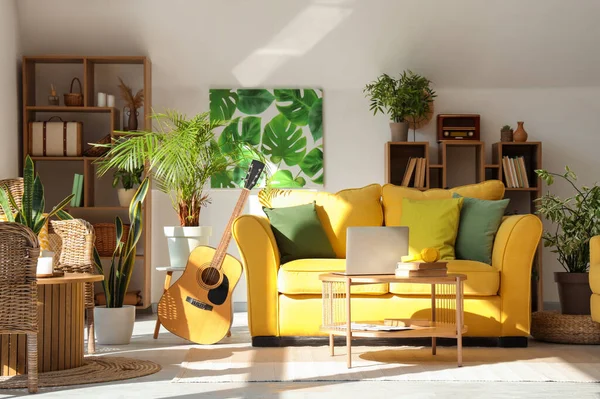 Interior of stylish living room with yellow sofa, laptop on coffee table and houseplants