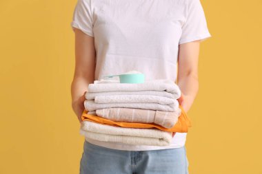 Sarı arka planda çamaşır deterjanı olan temiz havlu yığını tutan kadın.