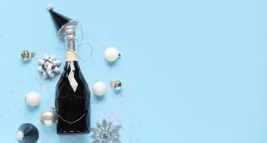 Şampanyalı kompozisyon, parti şapkası ve açık mavi arkaplan üzerine Noel süslemeleri.