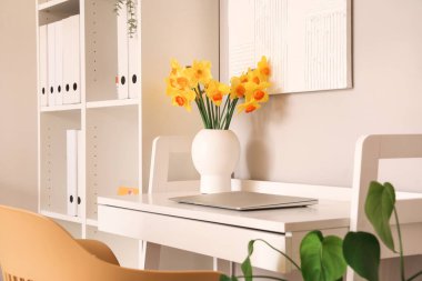 Modern dizüstü bilgisayarı ve gri duvarın yanındaki masada narsist çiçekleri olan rahat bir iş yeri.