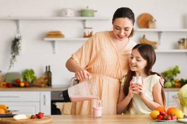 Küçük kızıyla birlikte genç bir kadın mutfaktaki cama taze meyve püresi döküyor.