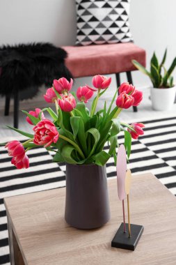 Vase with blooming tulip flowers on wooden coffee table in living room clipart