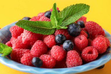 Sarı arka planda taze ahududu ve yaban mersini tabağı