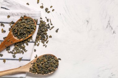 Beyaz arka planda kuru yeşil çay ve havlu ile ahşap kaşıklar.