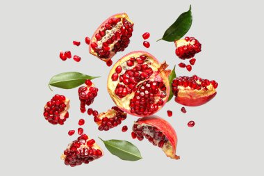 Tohumları ve yaprakları gri arkaplanda uçuşan taze narlar.