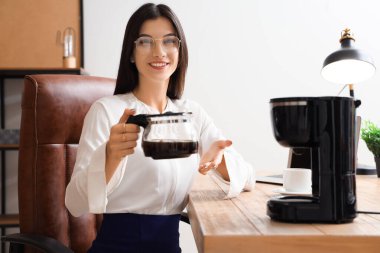 Ofisinde kahve makinesi olan genç bir iş kadını.
