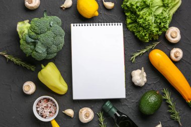 Siyah masanın üzerinde taze sebzeler olan boş bir defter.