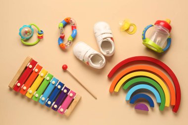 Emziği olan şık bebek ayakkabıları ve bej arka planda farklı oyuncaklar.