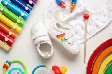 Önlüğü, oyuncakları, süt şişesi ve beyaz arka planda emziği olan şık bebek ayakkabıları.
