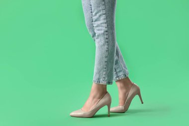 Yeşil arka planda, bej renkli yüksek topuklu genç kadın bacakları.