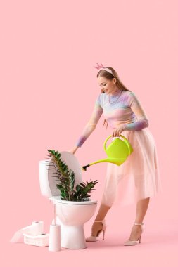 Sulama kabı olan genç bir kadın ve pembe arka planda klozete bitki.