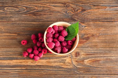 Taze ahududu ve ahşap arka planda yaprak dolu bir kase.