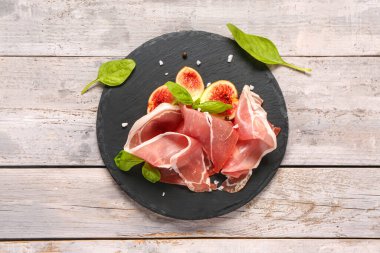Gri ahşap arka planda lezzetli prosciutto, fesleğen ve incir dilimleri olan bir tahta.