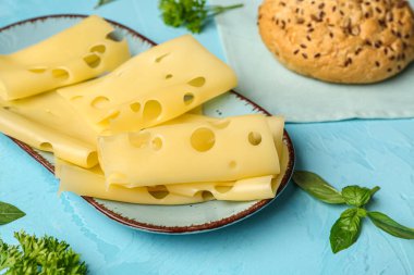 Lezzetli peynir dilimleri, fesleğen yaprakları ve mavi arka planda çörekler, yakın plan.