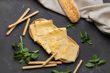 Lezzetli peynir dilimleri, fesleğen yaprakları ve koyu arkaplanda İtalyan Grissini tablosu.