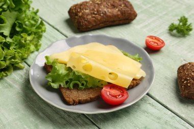 Peynirli lezzetli sandviç, yeşil ahşap arka planda marul ve domates, yakın plan.