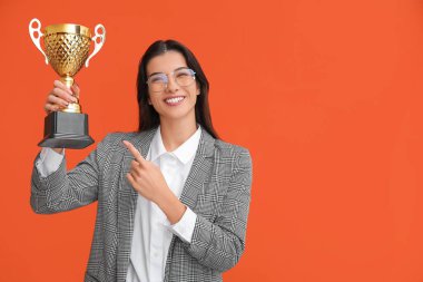 Genç iş kadını turuncu arka plandaki altın bardağı işaret ediyor.