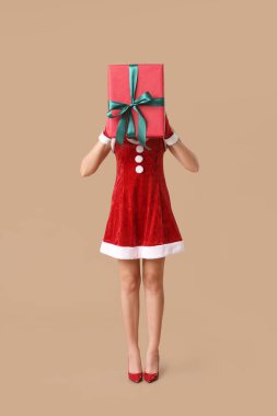Noel Baba kostümlü, kahverengi arka planda Noel hediyesi kutusu olan genç bir kadın.