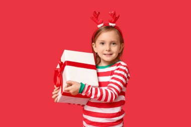 Kırmızı arka planda Noel hediyesi olan pijamalı şirin bir kız.