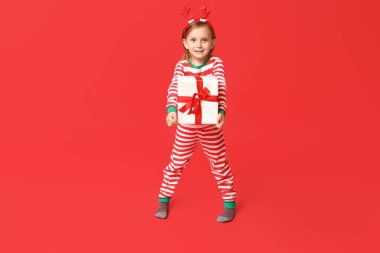 Kırmızı arka planda Noel hediyesi olan pijamalı şirin bir kız.