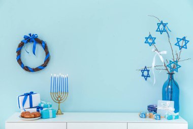 İçinde menorah, dreidels, sufganiyots ve mavi duvarın yanında hediye kutuları olan beyaz dolap. Hanuka kutlaması