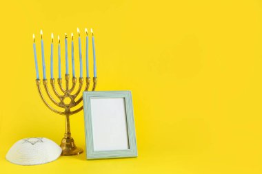 Mum yakan Menorah, boş resim çerçevesi ve sarı arkaplanda Hanuka kutlaması için kippah.